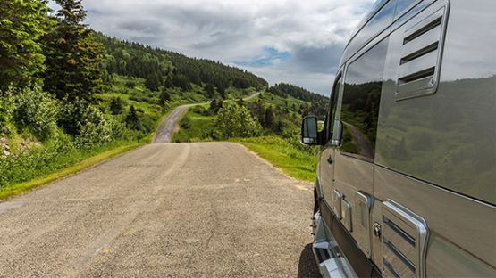 Motorhome on a dirt road with trees in the background.