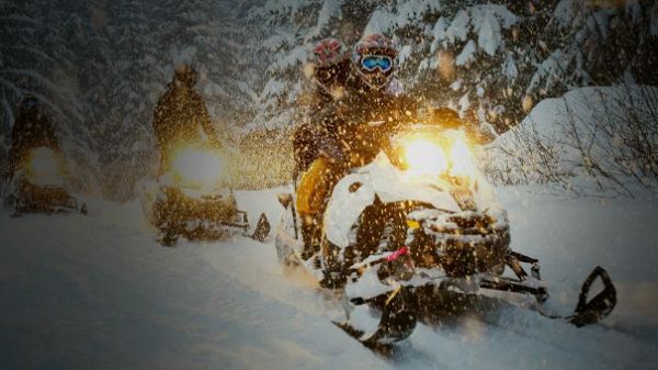 A group on snowmobiles on trail with falling snow