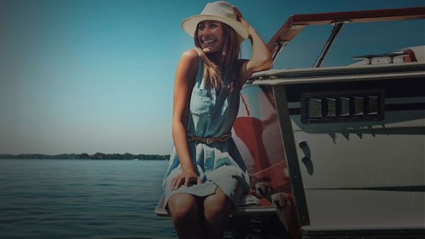 Young lady sitting on the side of boat holding onto hat