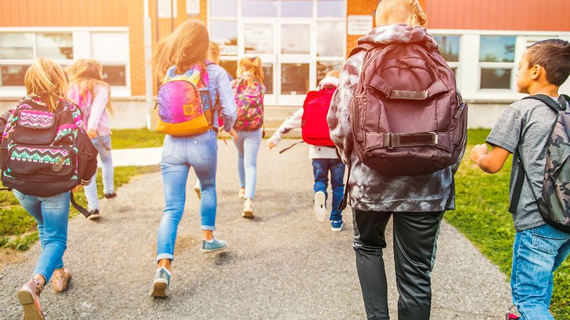 Des élèves courent en direction d’une école 