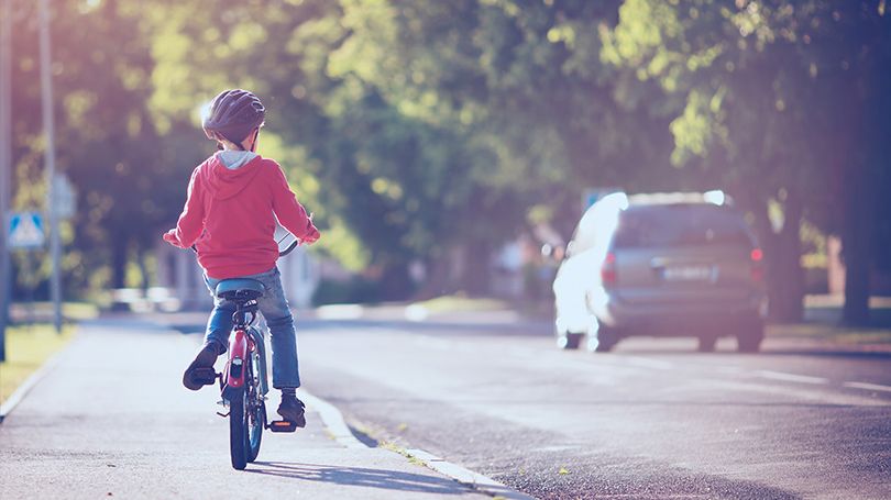 Un jeune enfant circule à bicyclette, sur le bas-côté d’une rue, tout près d’un véhicule