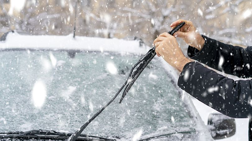 Person getting their car ready for the winter in snowy weather