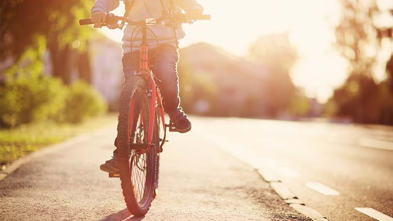 Un enfant circule à bicyclette, sur le bas-côté d’une rue, en route vers l’école