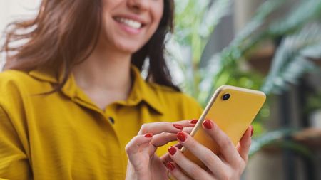 A woman smiling and downloading the Aviva Journey app onto her cellphone.