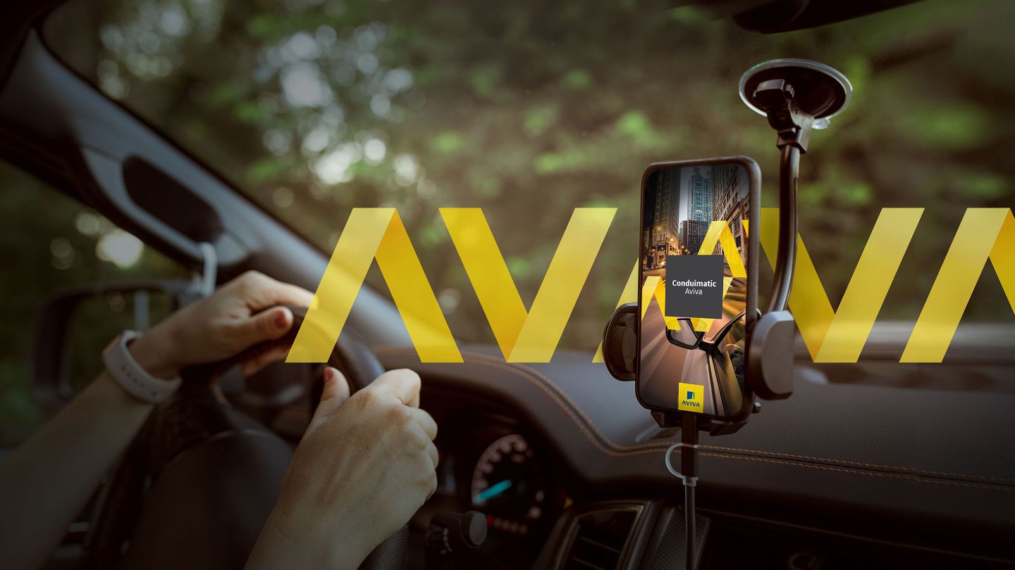 Gros plan de mains posées sur le volant et vue sur un téléphone intelligent monté sur le pare-brise et affichant l’écran d’accueil de l’appli de télématique Conduimatic Aviva