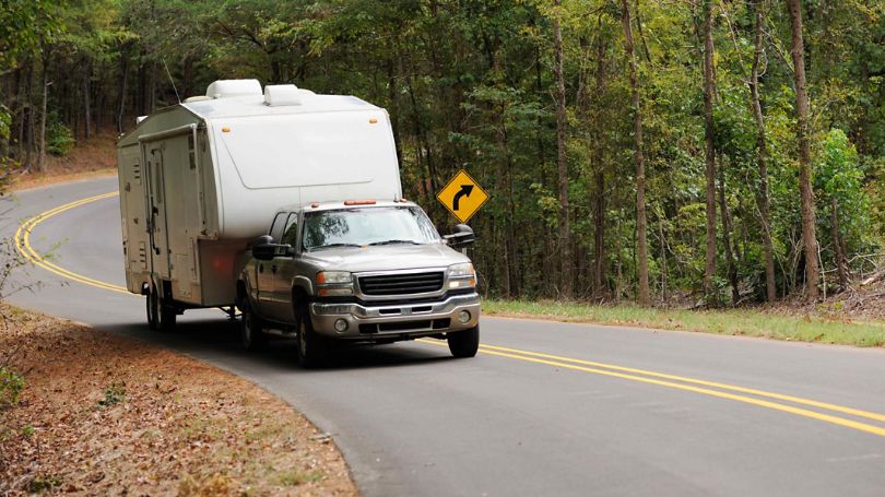 A truck pulling an attached travel trailer down a windy road.