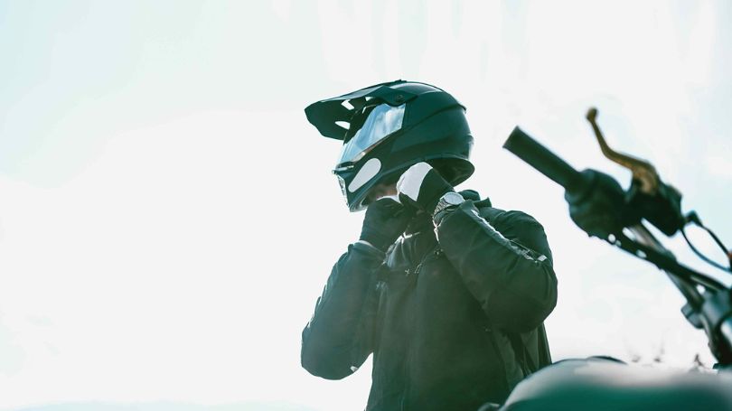 Un motocycliste ajustant son casque et s’apprêtant à partir. 