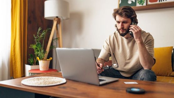 A photo of a late 20’s man sitting on a sofa with a laptop.