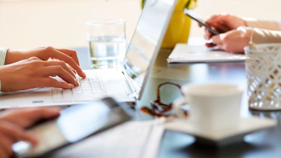 A close up image of a group of people using their computers and smart phones in a coffee shop.