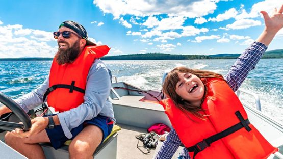 Father and daughter wearing life jackets on a small boat enjoying a day out on the water.