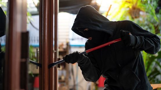 Individual, completely dressed in black, with hood and mask, breaking into home.