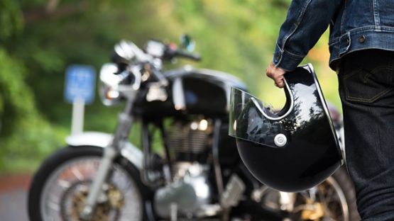 A close up image of a rider walking towards a motorcycle with helmet in hand