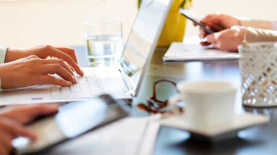 A close up image of a group of people using their computers and smart phones in a coffee shop. 