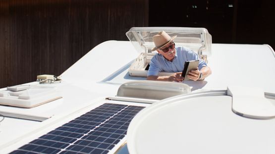 A senior man testing the solar panels atop his camper van with a tablet.