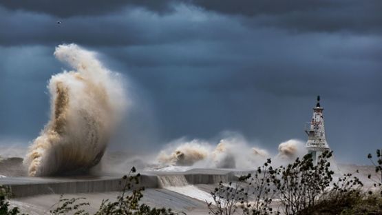 A stormy coastline with waves crashing the rocks in front of a lighthouse