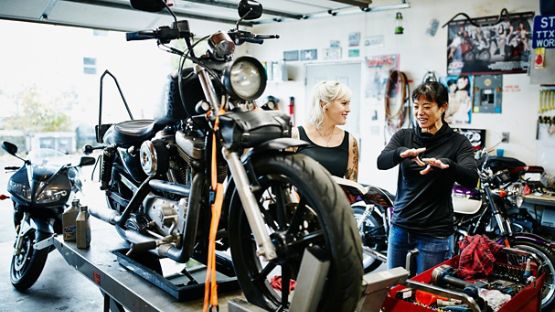 Two female mechanics discussing while working on motorcycles in a garage.