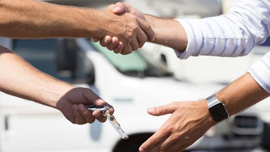 Close up of a handshake and key exchange with motor vehicles in the background.