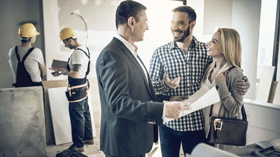 A couple speaking with an insurance representative about a claim with inspectors in the background assessing the home.