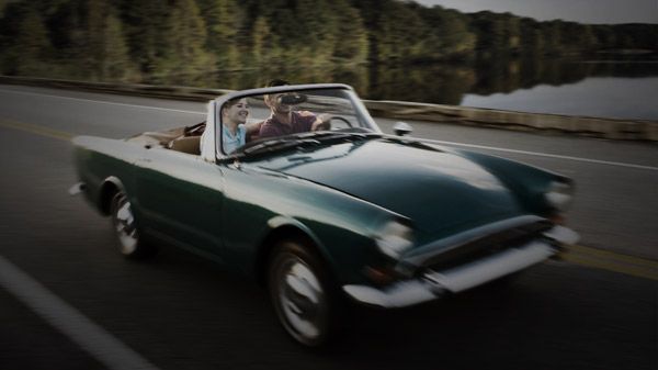 Two people driving on highway in collector car