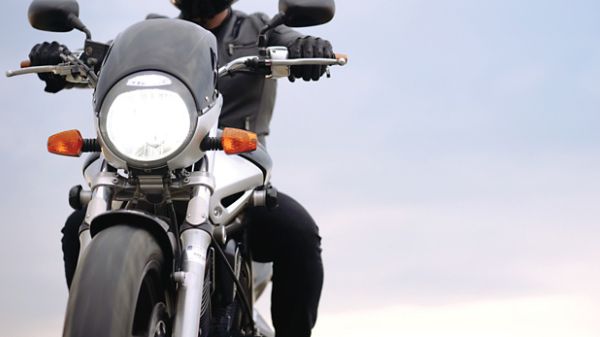 A crop shot of a biker sitting on a motorcycle at sunset