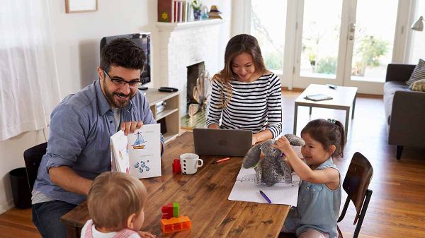 Mère qui regarde sa fille dessiner dans la salle familiale pendant que son père et son frère les regardent en arrière-plan.