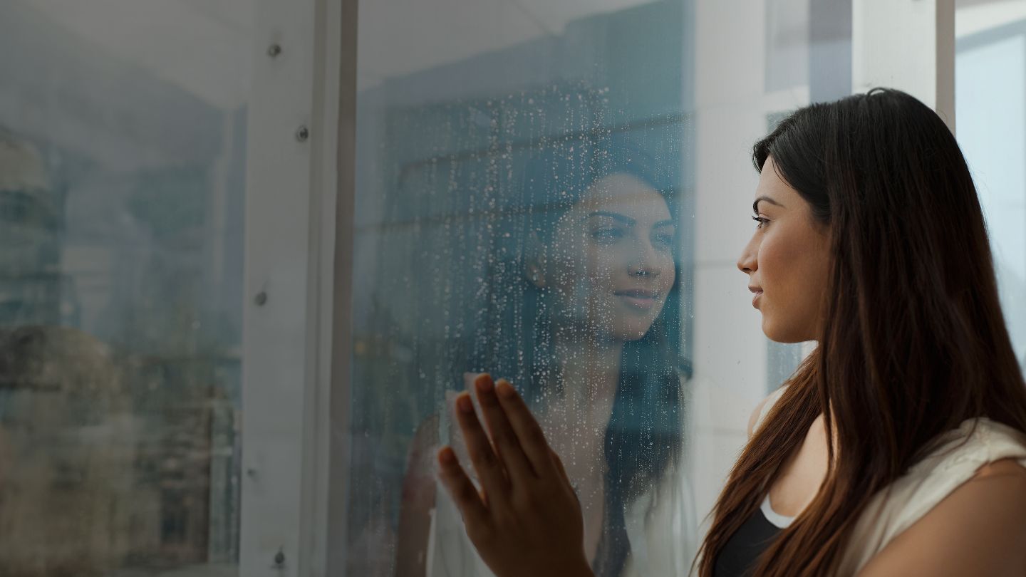 A woman at home watching the rain through her window.